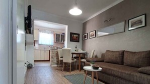 A modern living room with a brown sofa, a dining area with a table and chairs, and a kitchen in the background. - Holiday apartment with balcony and TV (Medulin)
