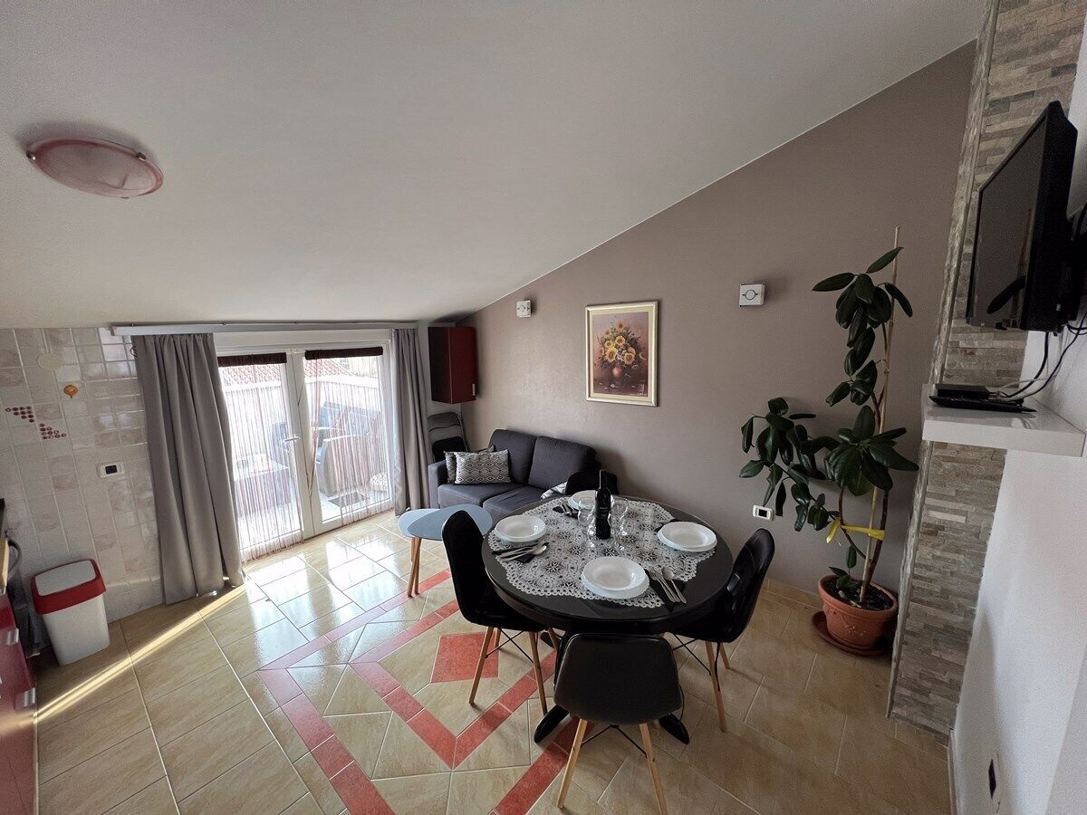 Un coin repas avec une table ronde dressée pour quatre personnes, un canapé, un téléviseur fixé au mur et une plante en pot.