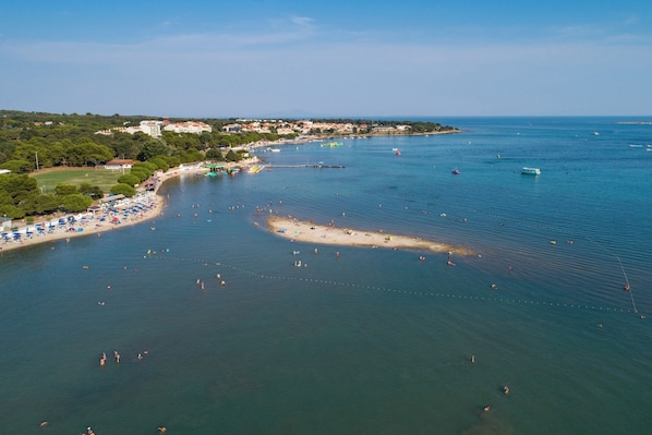 An aerial view of a coastal area with a beach, boats, and a clear sky.