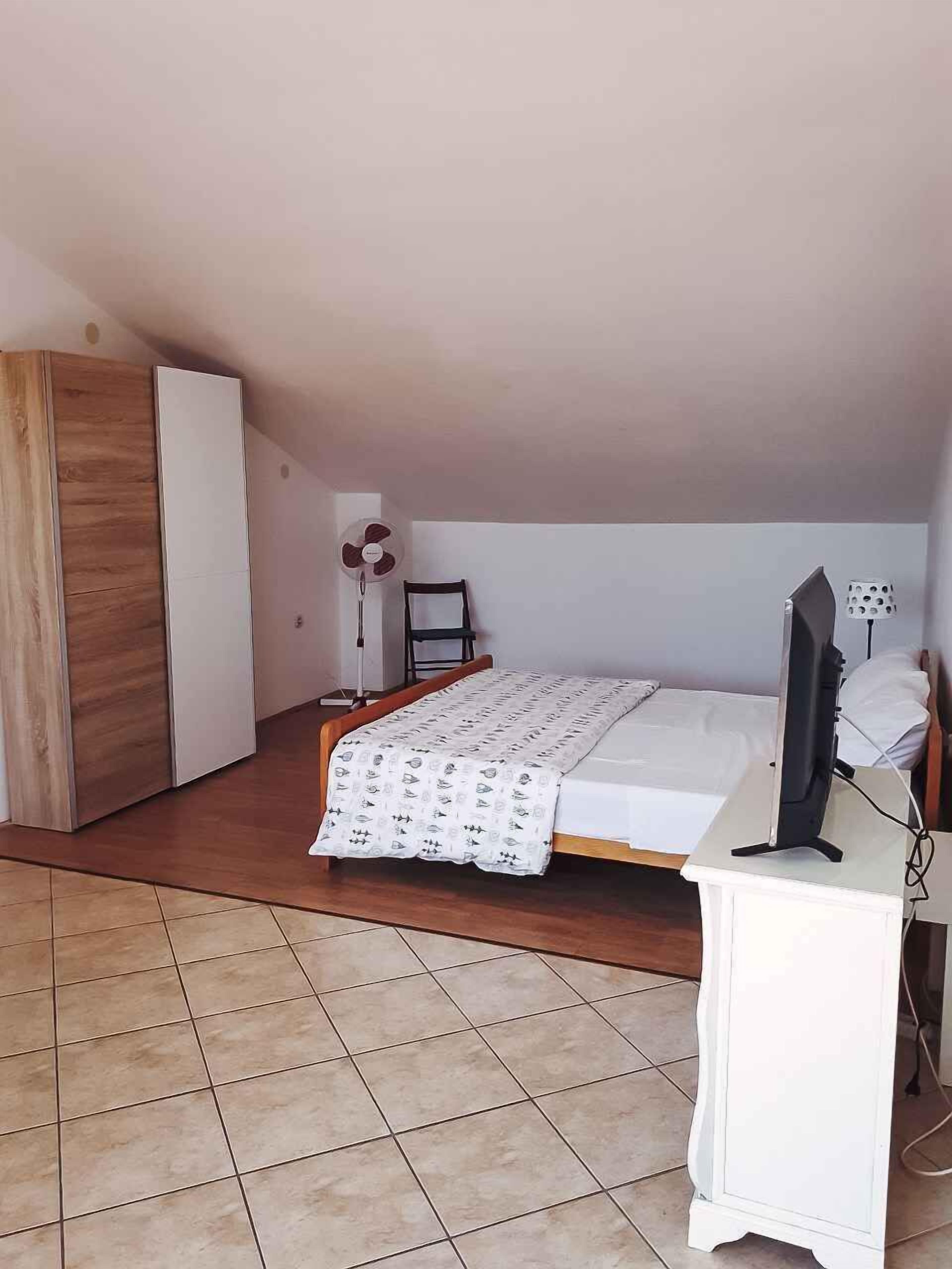 Ein Schlafzimmer mit einem Bett, einem Schreibtisch mit Computer, einem Kleiderschrank und einem Ventilator.