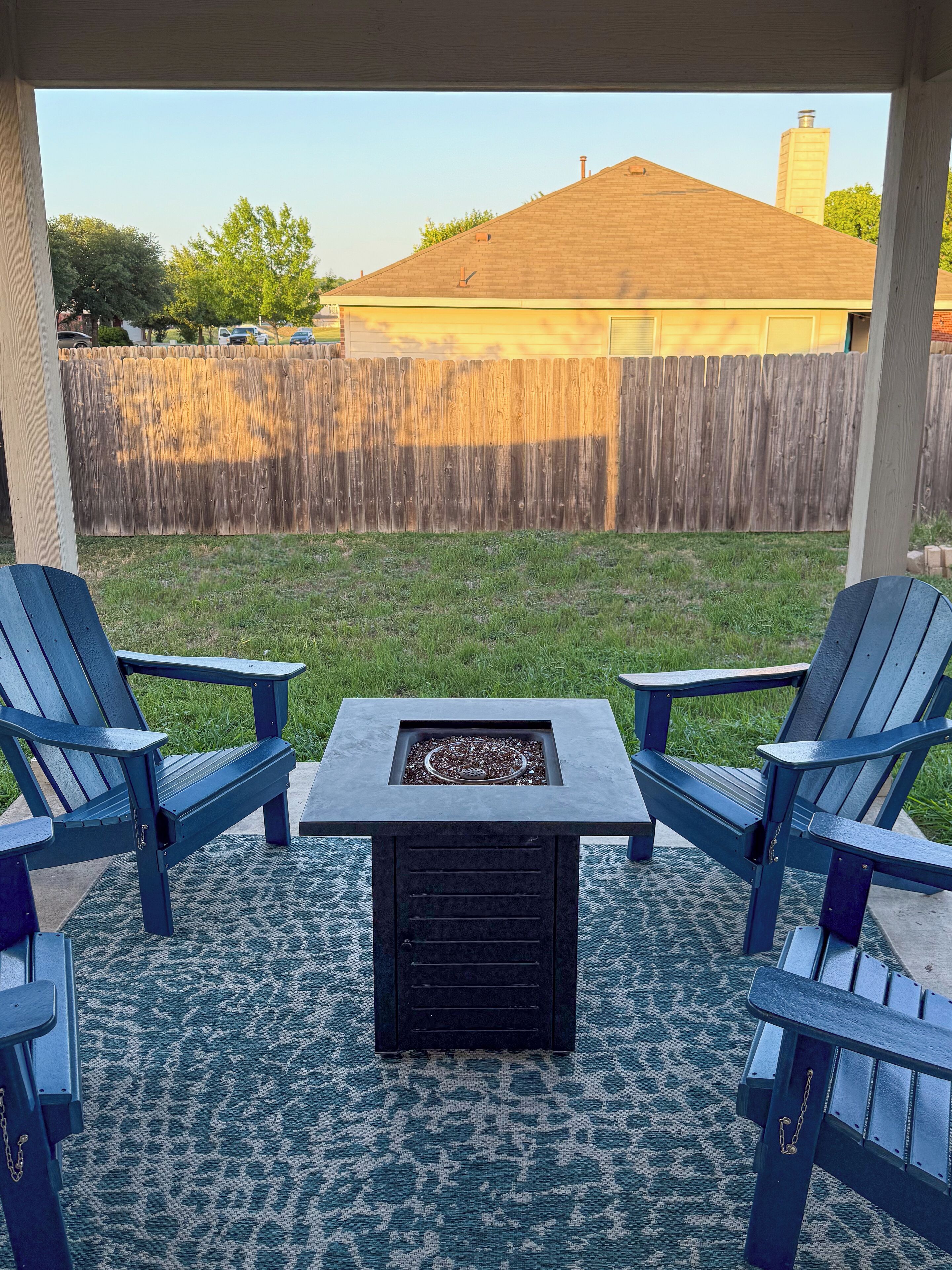 A covered patio area with two Adirondack chairs facing a square fire pit.