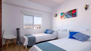 A hotel room with two beds, a chair, a heater, a window with a view, and a colorful painting on the wall. - Strand II by Interhome (Jávea)