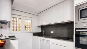 A modern kitchen with white cabinetry, a black countertop, a built-in oven, and a window with decorative bars. - Strand II by Interhome (Jávea)