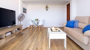 A living room with a TV, a fan, a table with a candle, and a sofa with blue pillows. - Strand II by Interhome (Jávea)