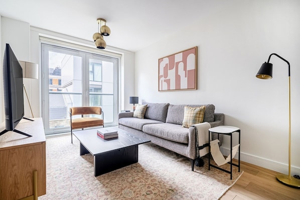 A modern living room with a sofa, coffee table, and a chair. There is a TV, a lamp, and a painting on the wall.
