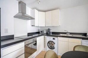 Une cuisine moderne équipée d’un four encastré, d’un micro-ondes et d’un lave-linge, ainsi que d’un évier et d’un coin repas.