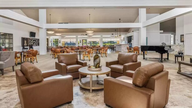 Eine geräumige Lobby mit Ledersofas, einem Flügel und einem Essbereich mit Tischen und Stühlen.