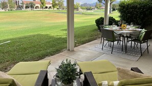 Eine überdachte Terrasse mit Esstisch für zwei Personen mit Blick auf einen gepflegten Rasen und einen Golfplatz.