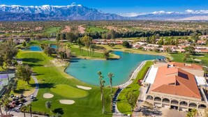 Ein Golfplatz mit einem See, ein Gebäude mit rotem Dach und Berge im Hintergrund.