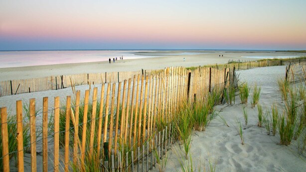 A beach with a wooden fence and sand dunes.