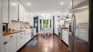 A modern kitchen with white cabinetry, a stainless steel refrigerator, and a dining area with a view of greenery.