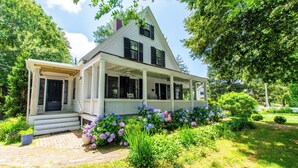 A two-story house with a porch, surrounded by lush greenery and flowering plants.
