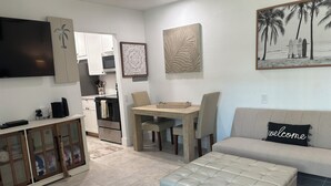 A modern living room with a sofa, ottoman, and a dining area with chairs and a table.