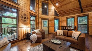 Eine geräumige Hütte mit Holzwänden und großen Fenstern, ein gemütlicher Wohnbereich mit Sofa und Couchtisch sowie ein Essbereich mit Tisch und Stühlen.