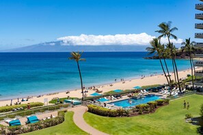 A resort with a pool, beach, and palm trees.