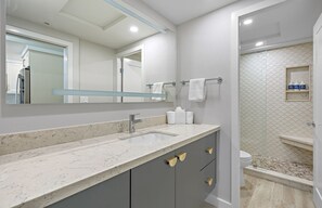 A modern bathroom with a marble sink, a large mirror, and a shower area with a tiled wall.