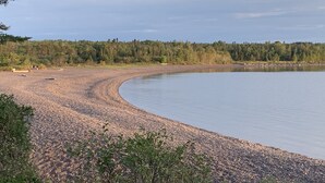 Ein Kiesstrand mit einem stillen See, umgeben von dichtem Wald.