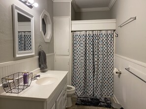 A bathroom with a white vanity, a toilet, a shower with patterned curtains, and a mirror above the vanity. - 2 BD / 2 BA  (Charlotte)