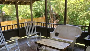 A covered outdoor seating area with a wooden table, two rocking chairs, and a patterned rug. - 2 BD / 2 BA  (Charlotte)
