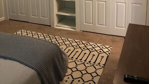 A room with a bed, a patterned rug, a wooden table, and a closet with shelves. - 2 BD / 2 BA  (Charlotte)