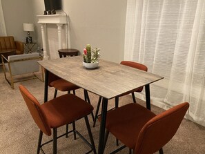 A dining area with a wooden table, four orange chairs, a small side table, a lamp, and a cactus plant. - 2 BD / 2 BA  (Charlotte)