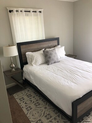 A neatly made bed with white bedding and patterned pillows, a bedside lamp, and a patterned rug on a carpeted floor. - 2 BD / 2 BA  (Charlotte)
