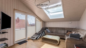 Et værelse med fjernsyn, sofa, lænestol, rampe og ovenlysvinduer.