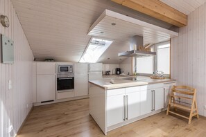 Una cocina moderna con armarios blancos, techo de madera y tragaluz.
