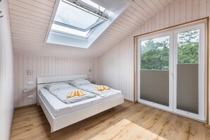 Un dormitorio con tragaluz, cama, puerta corredera de vidrio y suelo de madera.