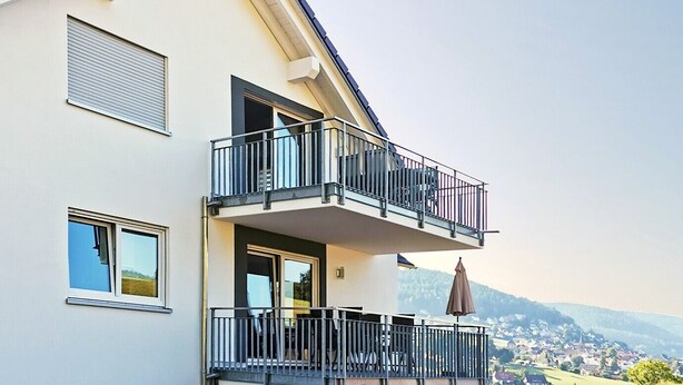 Ein zweistöckiges Haus mit Balkon, einem Essbereich mit Gartenmöbeln und Blick auf eine grüne Landschaft.