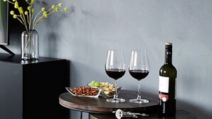 Een ronde tafel met een wijnfles, twee glazen en een schaal met lekkernijen.