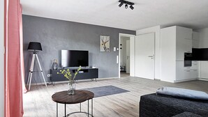 Een moderne woonkamer met een bank, salontafel, televisie en een keukenhoek.