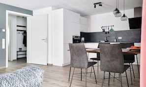 A modern kitchen with white cabinets, a dining table with chairs, and hanging kitchen utensils. - Apartment "Rehkitz" in Black Forest with Balcony & Wi-Fi (Baiersbronn)