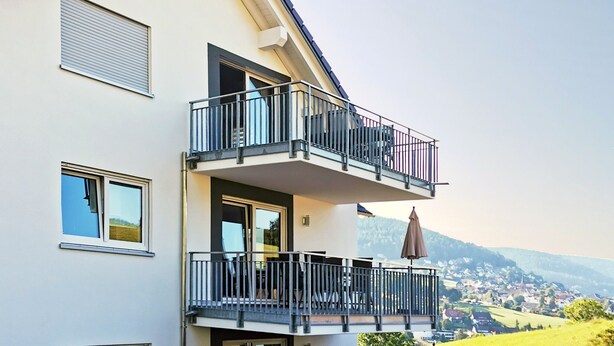 Un edificio de dos pisos con balcón, mobiliario exterior y vistas a un paisaje verde.