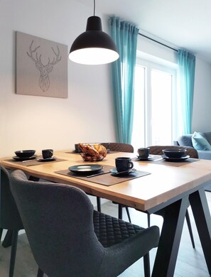 A dining area with a wooden table, black chairs, a black pendant light, and a window with curtains.