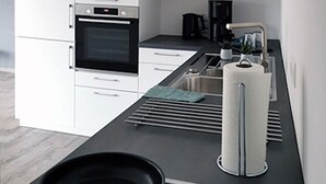 Una cocina moderna con armarios blancos, horno empotrado, cafetera y hervidor sobre la encimera.