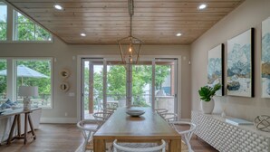 A dining area with a wooden table and white chairs, large windows, and a view of greenery outside. - Save 15% Off 4 Night Stay! Amazing Waterfall/Lake Views! Pool, Dock! (Vinita)