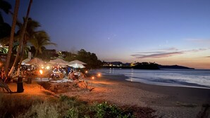 Un ristorante sulla spiaggia con posti a sedere all'aperto, palme e vista sull'oceano al tramonto.