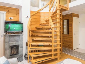 Una escalera espiral de madera en una habitación con chimenea, televisión y una puerta.