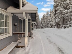 Una casa cubierta de nieve con un porche y un sendero que lleva a un bosque.