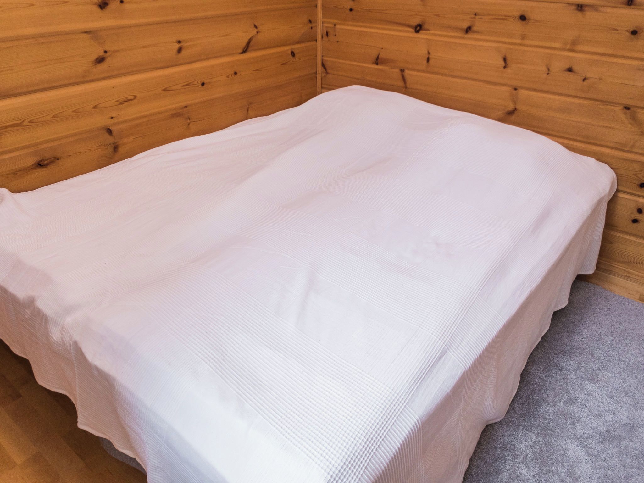 Eine kleine Holzhütte mit einem Einzelbett, Holzvertäfelung und einem grauen Teppich.