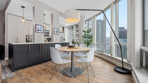 Et moderne køkken med spiseplads, med et rundt bord, hvide stole og et stort vindue der giver udsigt over byen.