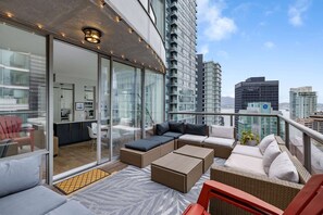 En moderne balkon med fletningsmøbler, glasdøre der fører til et indre rum, og udsigt over byen.