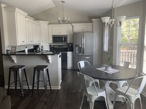 A modern kitchen with white cabinetry, stainless steel appliances, a central island with stools, and a dining area with a glass table and chairs.