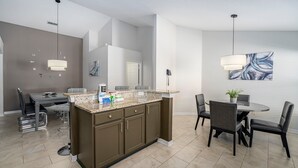 A modern kitchen with a central island, dark cabinetry, and a dining area with a round table and chairs. - Pool Home with Spa & Games Room in Gated Community Near WDW (Davenport)