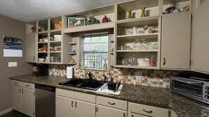 A kitchen with beige cabinets, a granite countertop, a dishwasher, a window with a view, and a calendar on the wall.
