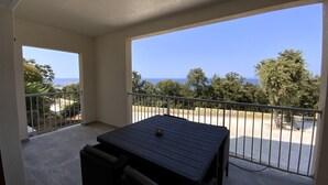 A balcony with a table and chairs, offering a view of the sea and trees. - Residence La Listrella apt 2 (Monticello)