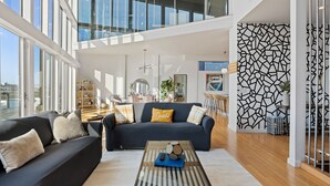 A spacious living room with a dark blue sofa, a coffee table, and a view of the city through large windows. - Nashville Skyline Views - 3BR/3BA, 5 Mins to Downtown (Nashville)