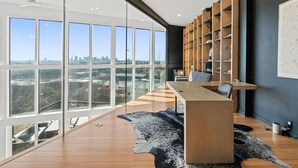 A modern office with a long wooden table, a large bookshelf, and a city view through floor-to-ceiling windows. - Nashville Skyline Views - 3BR/3BA, 5 Mins to Downtown (Nashville)