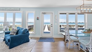A room with a view of the beach, a glass table, wicker chairs, a blue sofa, and a white rug.